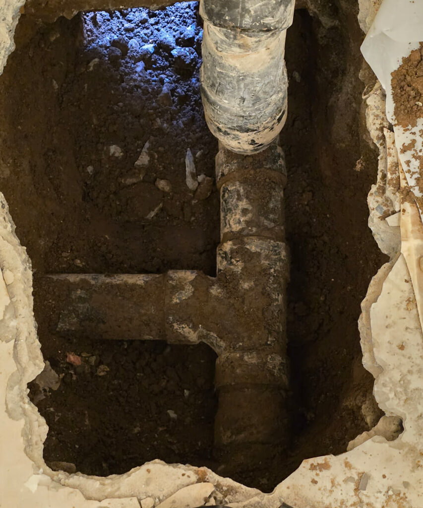 An excavated area showing old, dark plumbing pipes embedded in dirt