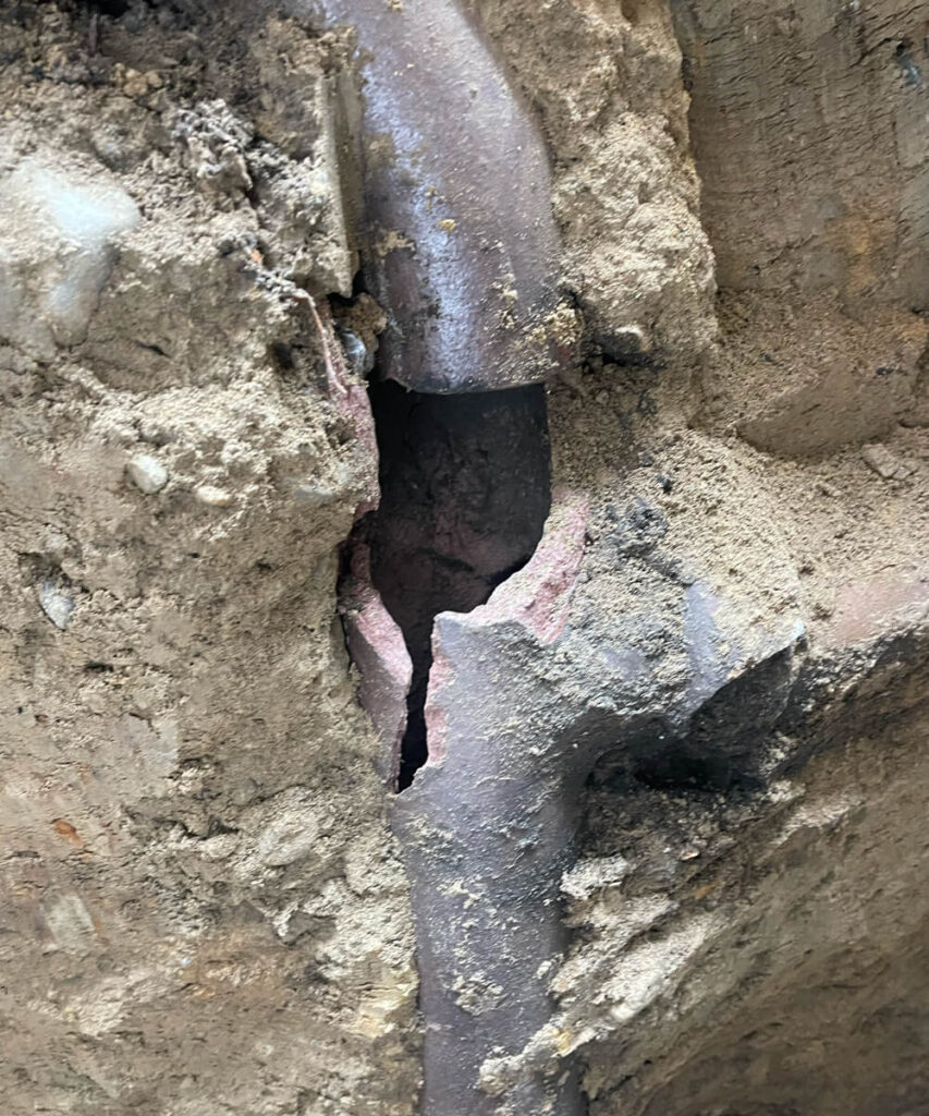 A severely cracked and broken metal pipe exposed in dirt