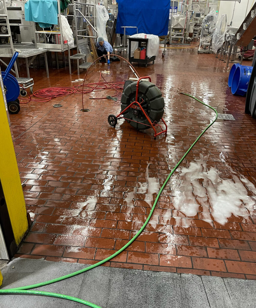 An industrial facility floor being cleaned with a sewer jetting machine and hoses