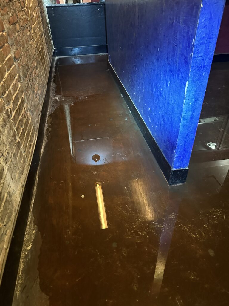 A dark, reflective floor covered by standing water in an indoor space. 