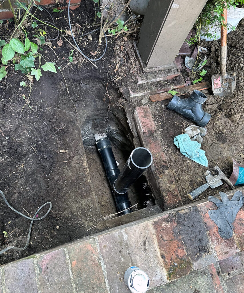 An outdoor trench revealing new black PVC pipes being installed for a sewer line repair