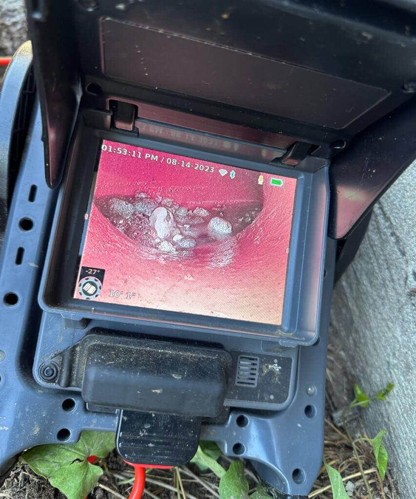 A drain camera monitor displaying the inside of a pipe with white debris