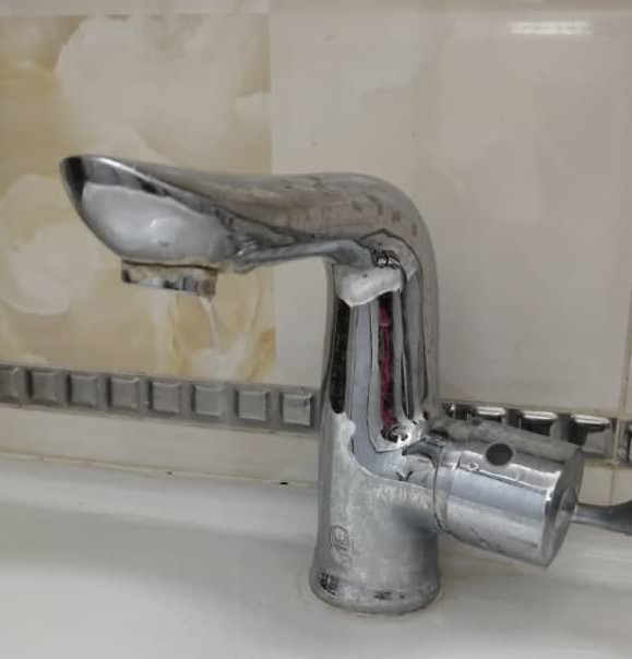 A chrome faucet, visibly dripping water into a white sink