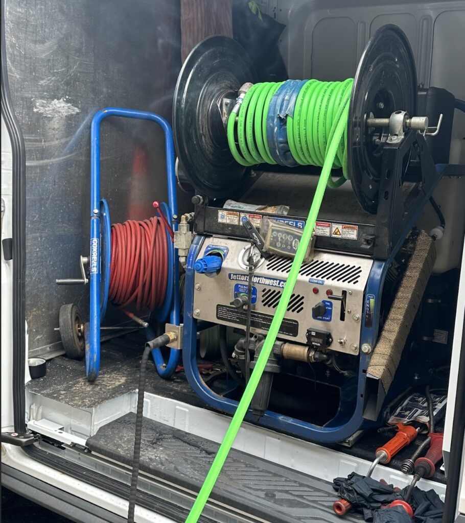 Drain cleaning equipment in a service van, featuring large green and red hose reels with a central machine