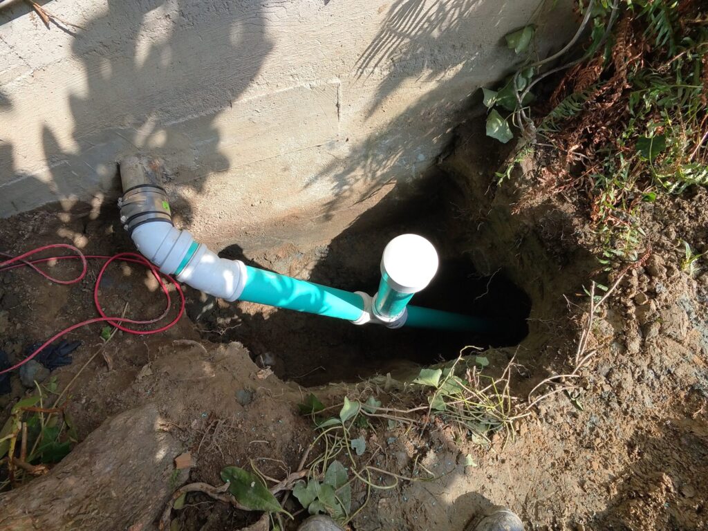 A new turquoise sewer pipe with white fittings extending from a wall into an excavated trench