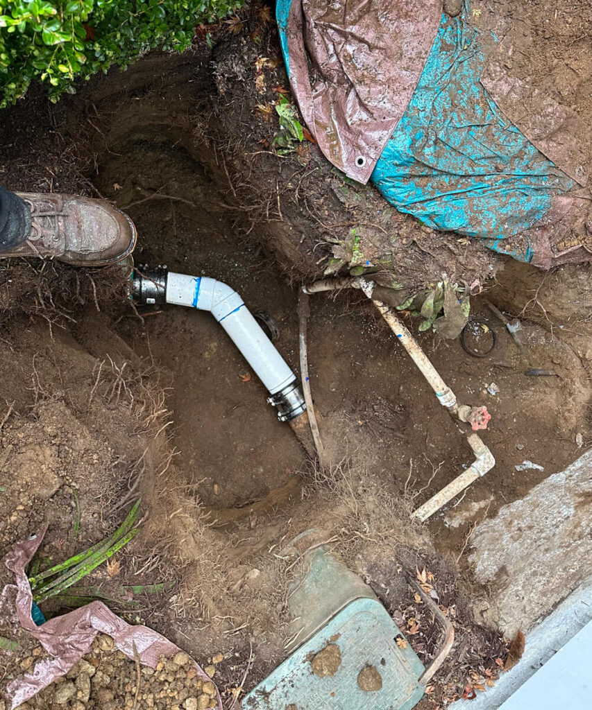 An excavation revealing a newly installed white PVC pipe connected to older lines for a sewer service repair