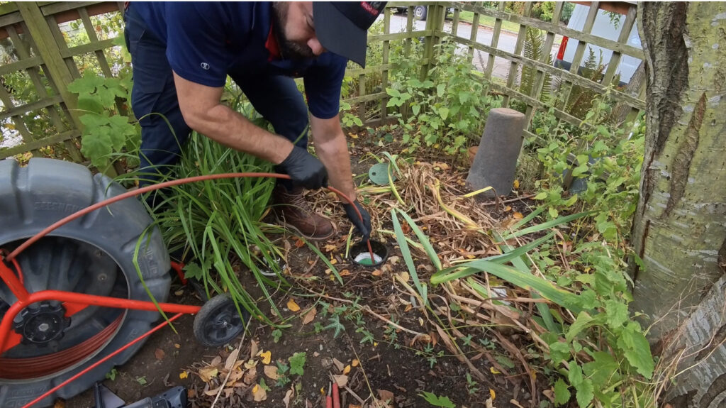 A plumber wearing a dark blue shirt and gloves performing a camera inspection